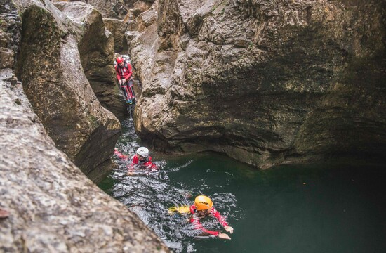 Personen beim Canyoning in einer felsigen Schlucht, ausgerüstet mit Helmen und Neoprenanzügen, schwimmen durch klares Wasser.