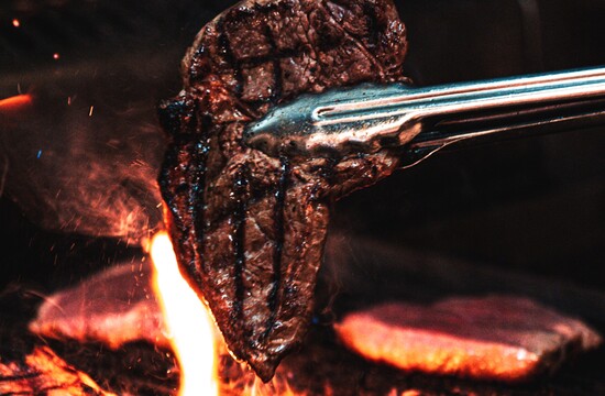 Ein saftiges Steak wird mit einer Zange über einer offenen Flamme auf einem Grill gegrillt.